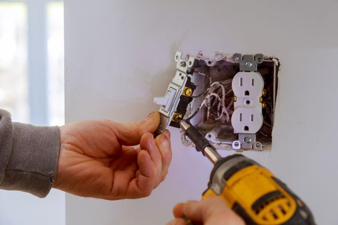 Person using drill to remove light switch from outlet