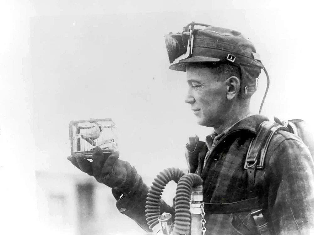 Coal miner holding a canary in a small cage outside of the coal mines